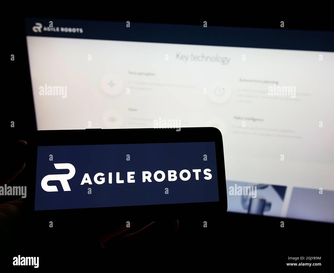 Person, die das Mobiltelefon mit dem Logo des deutschen Technologieunternehmens Agile Robots AG auf dem Bildschirm vor der Business-Webseite hält. Konzentrieren Sie sich auf die Telefonanzeige. Stockfoto