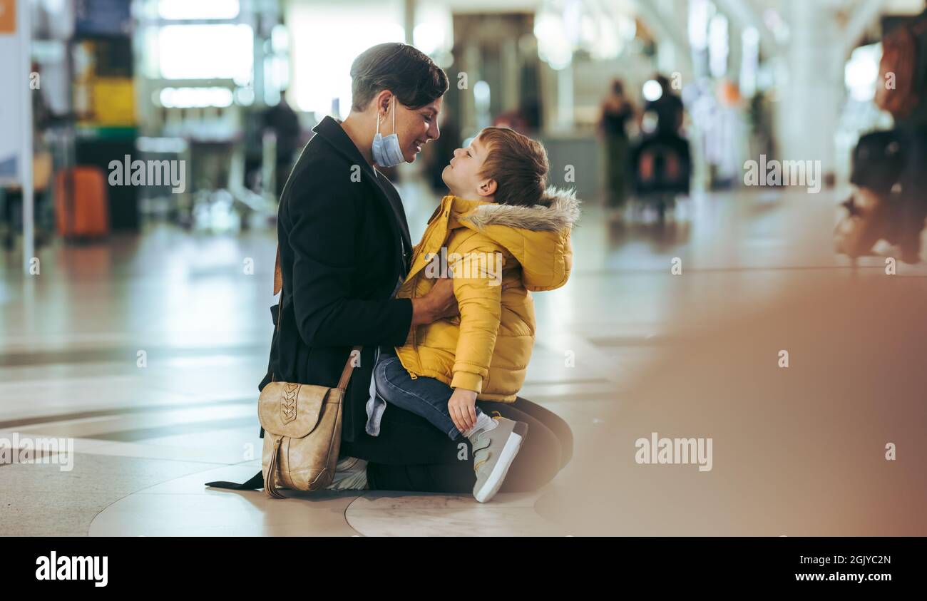 Liebevolle Mutter und Sohn am Flughafen. Mutter in Gesichtsmaske, die ihren Sohn festhält, nachdem sie während einer Pandemie aus dem Ausland angekommen war. Stockfoto