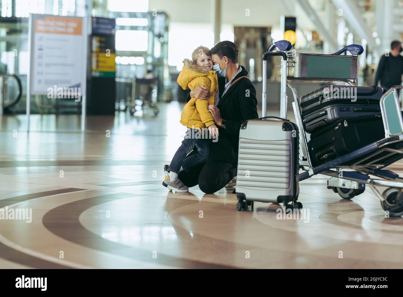 Frau mit ihrem Sohn, indem sie während einer Pandemie auf den Knien am Flughafen saß. Mutter und Sohn warten während des Covid-19-Ausbruchs auf dem Flughafen. Stockfoto