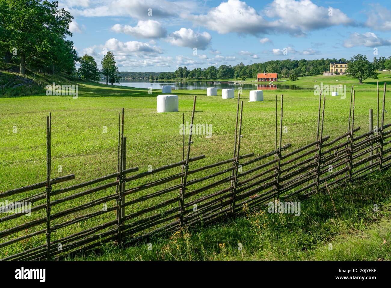 Kleiner Siedlungsbauernhof in Südschweden an einem schönen sonnigen Sommertag. Urlaub in der schwedischen Landschaft. Vintage Zaun und weiße Heystacks. Stockfoto