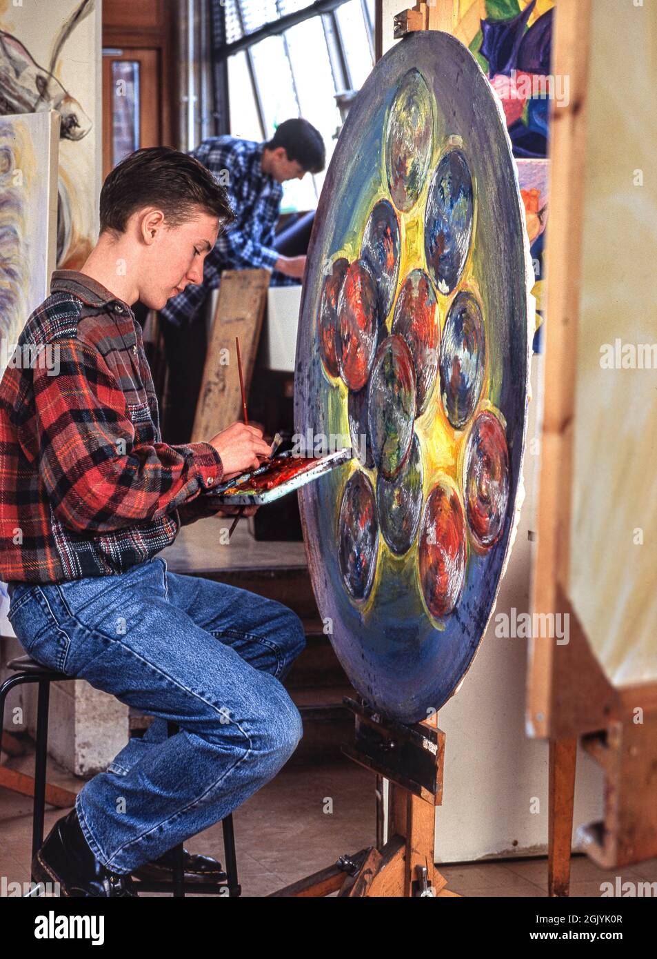 Kunstklasse mit einem Schüler mit 15-17 Jahren Oberstufe, der seinen expressiven, modernen, kreisförmigen, in Öl gemalten Kunstwerken einen letzten Schliff verleiht Stockfoto