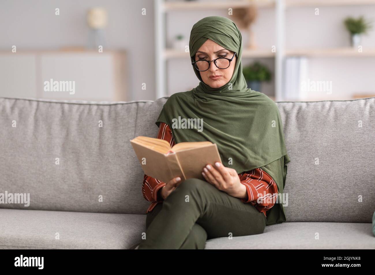 Ältere Muslimische Weibliche Lesebuch Tragen Brillen Sitzen Zu Hause Stockfoto