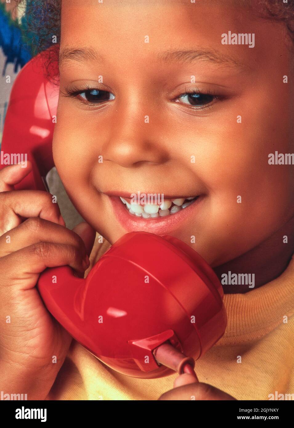 Kleinkind 4 Jahre altes Mädchen African Caribbean ziemlich niedlich glücklich lächelnd Gespräch auf ihrem roten Retro Vintage-Stil Telefon Hörer Stockfoto