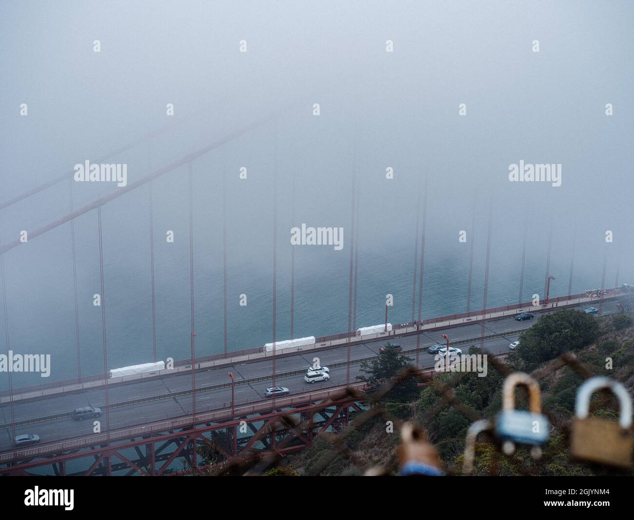 Golden Gate Bridge im typischen Sommernebel mit Autos, die unten vorbeifahren, gesehen hinter einem Zaun aus Liebesvorhängeschlössern Stockfoto