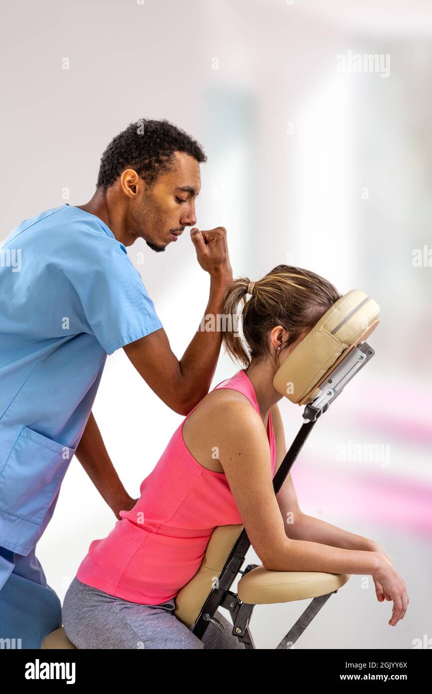 Physiotherapeut gibt einer Patientin, die in einem Massagesessel in der Klinik sitzt, eine Rückenmassage. Stockfoto