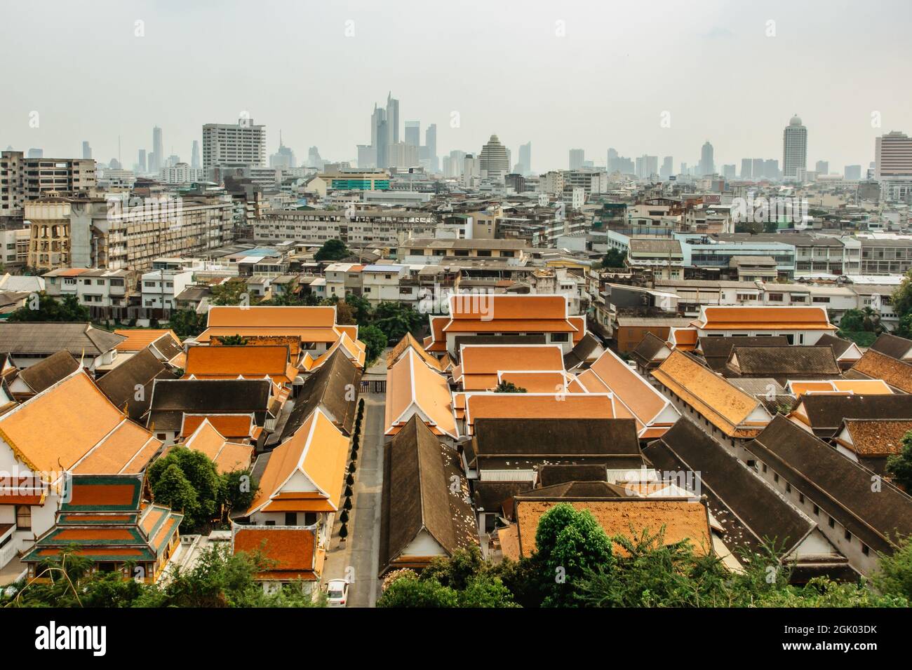 Panoramablick auf Bangkok vom Golden Mountain an bewölktem staubigen Tag, Thailand. Traditionelle thailändische Architektur von oben, moderne Wolkenkratzer im Hintergrund. Stockfoto