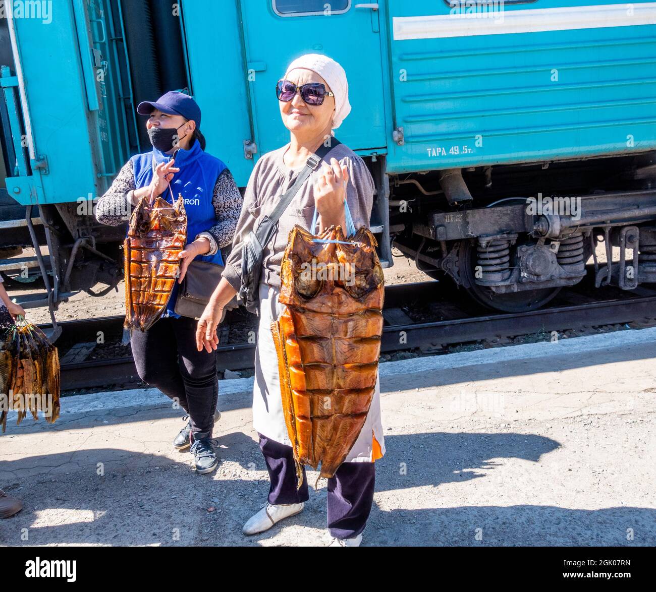 Frauen, die geräucherten Fisch auf der Haltestelle an die Zugpassagiere, Sary-Shagan Station, in der Nähe von Balkhash Lake, Kasachstan, Zentralasien, verkaufen Stockfoto
