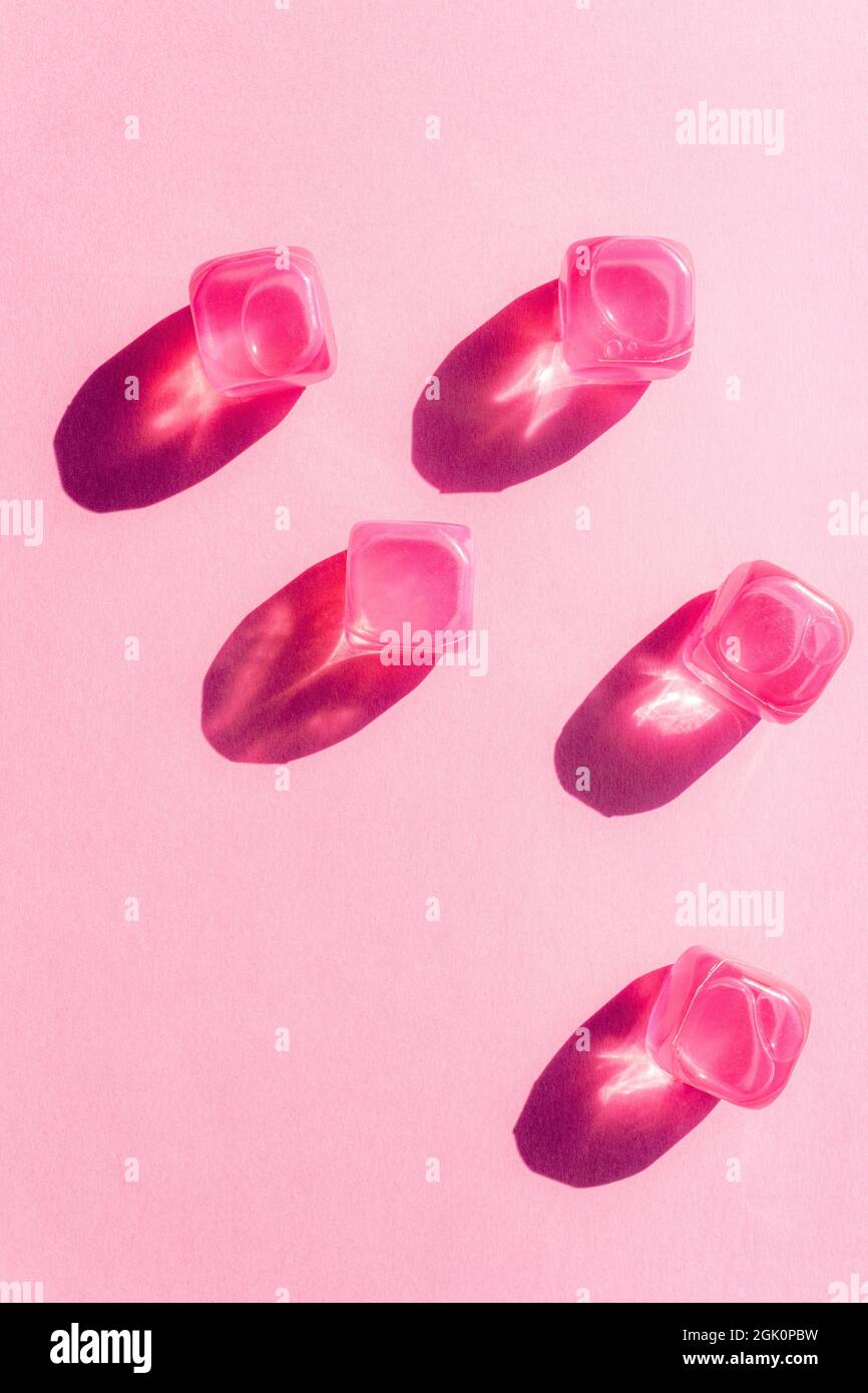 Kreatives Layout mit rosa Plastikwürfeln aus Eis in der Mittagssonne und harten Schatten im Hintergrund. Sommermockup. Flach liegend. Speicherplatz kopieren. Stockfoto