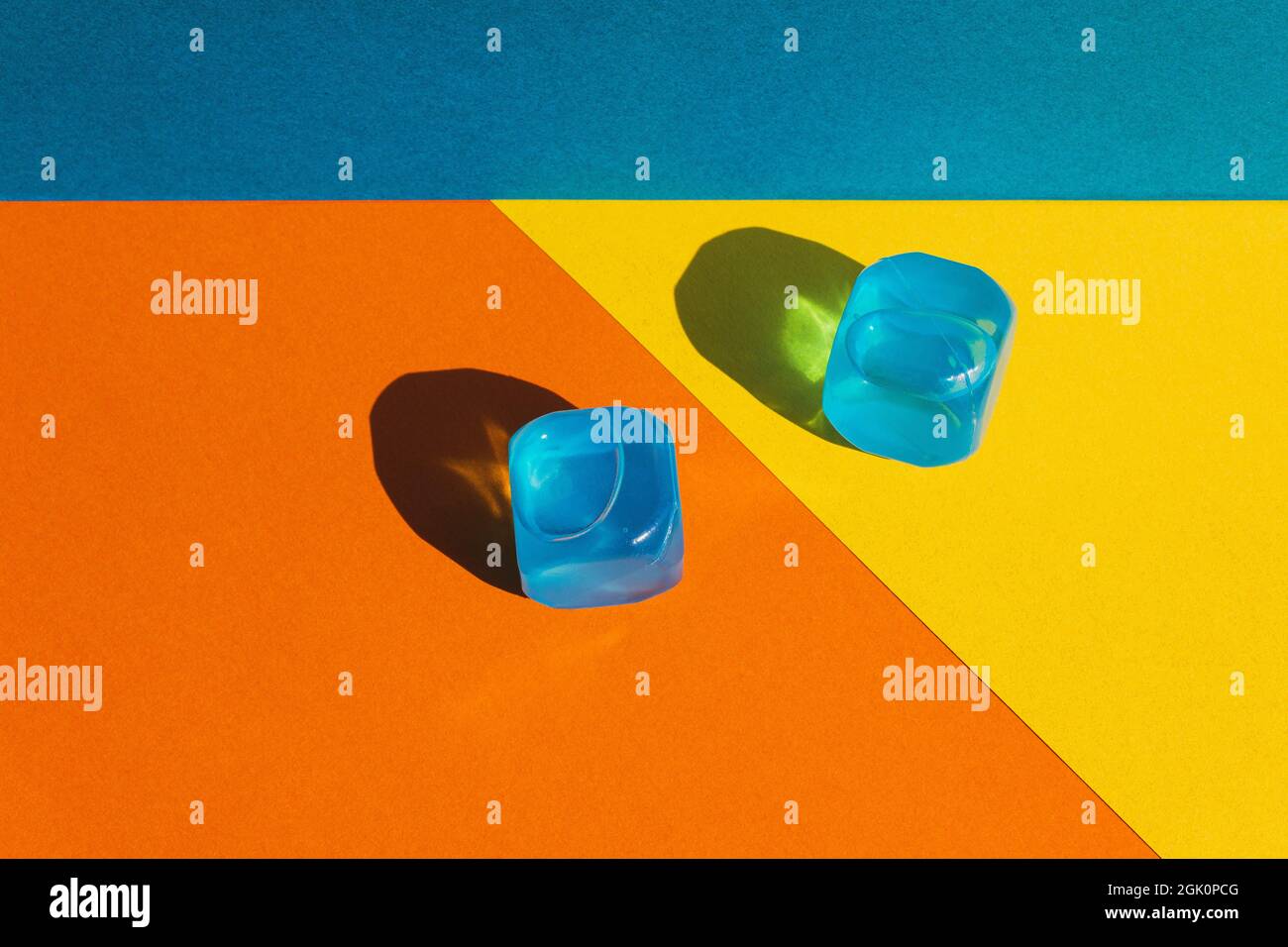 Kreatives Layout mit blauen Plastikwürfeln aus Eis in der Mittagssonne und harten Schatten im Hintergrund. Sommermockup. Flach liegend. Speicherplatz kopieren. Stockfoto