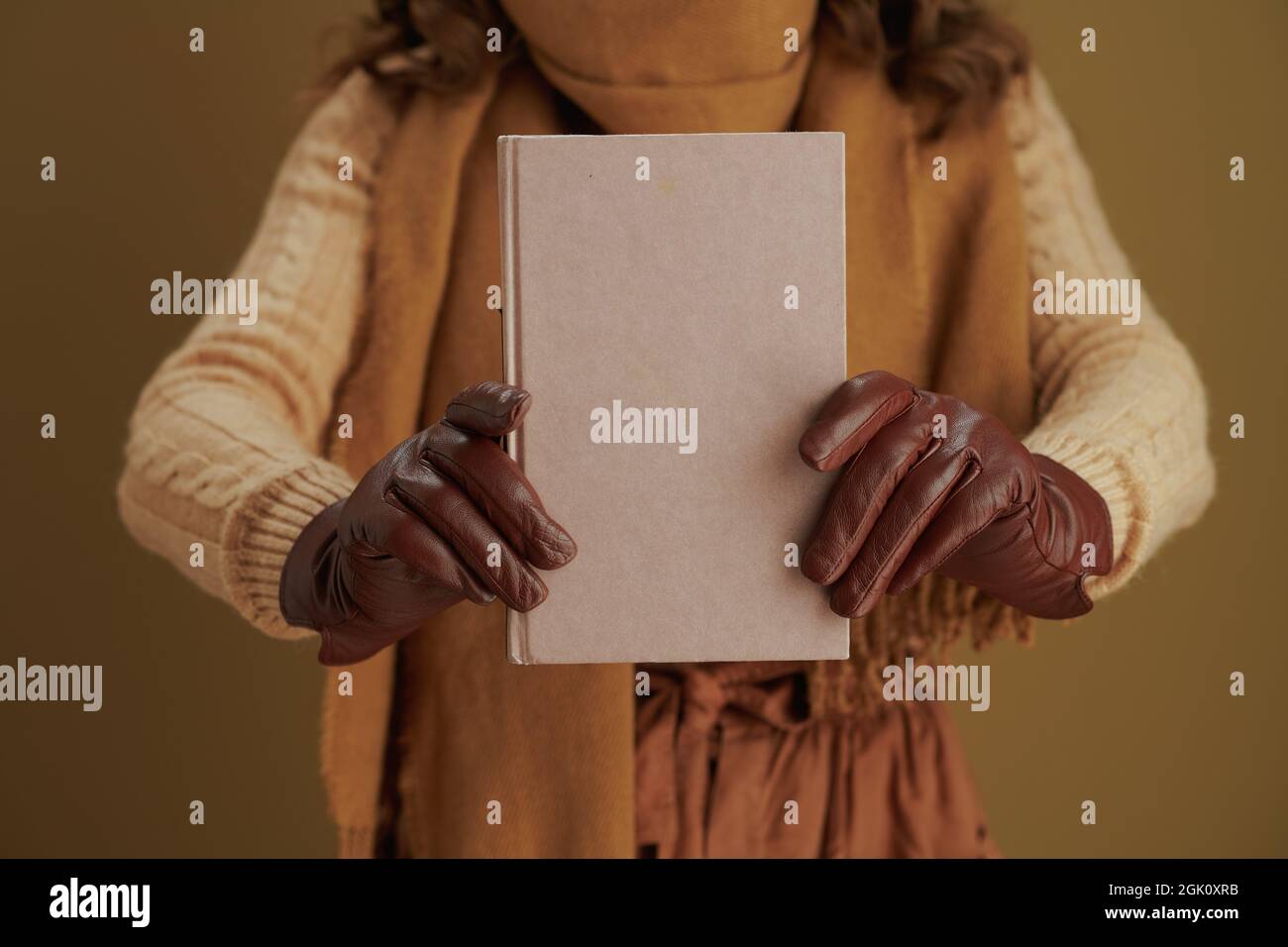 Hallo Herbst. Nahaufnahme einer Frau mittleren Alters mit Buch und Lederhandschuhen vor bronzefarbenem Hintergrund. Stockfoto