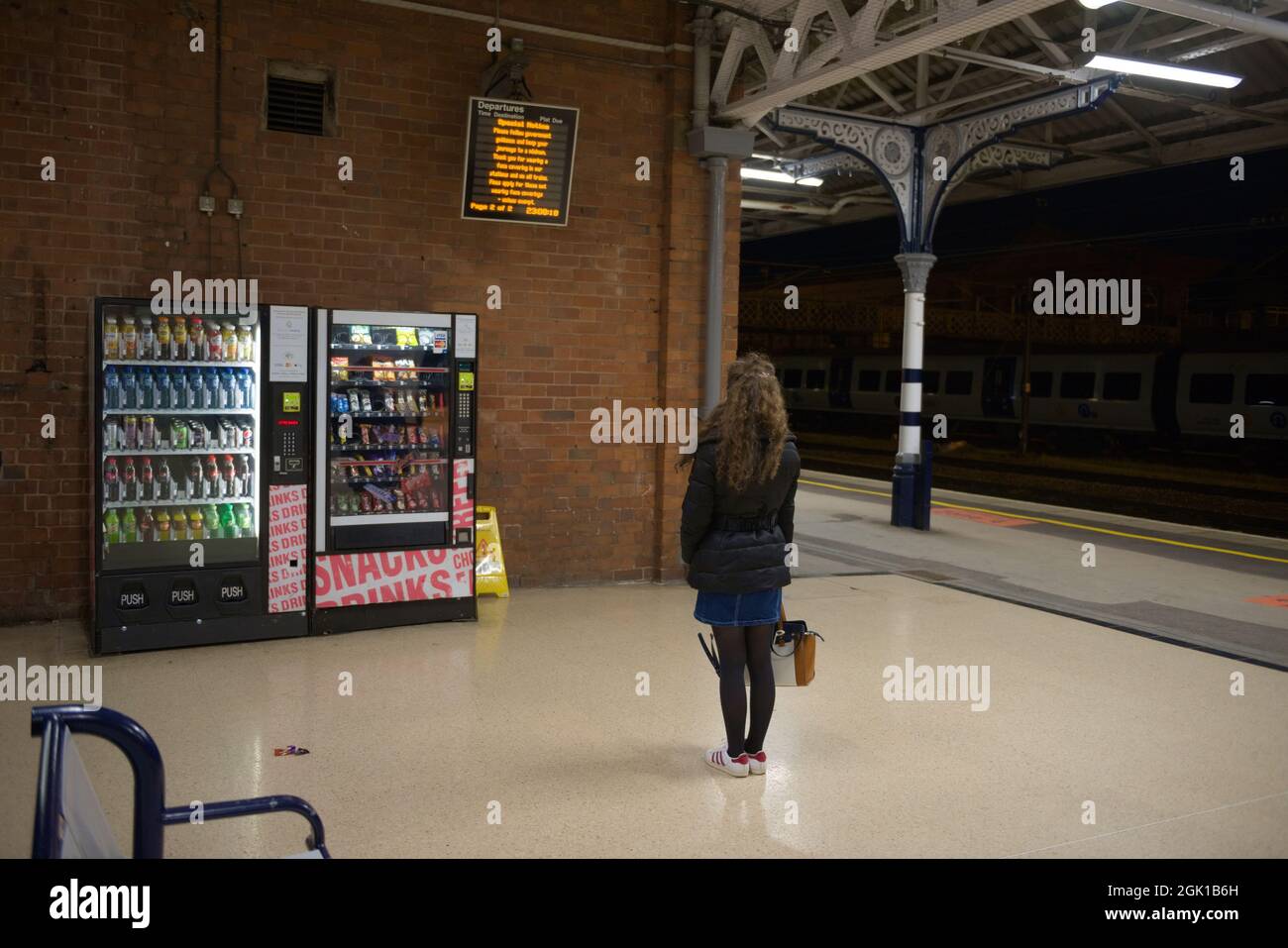 Doncaster, Großbritannien, 22. Mai 2021: Eine junge Frau mit Mantel, Rock und Handtasche wartet nachts am Bahnhof von doncaster Stockfoto