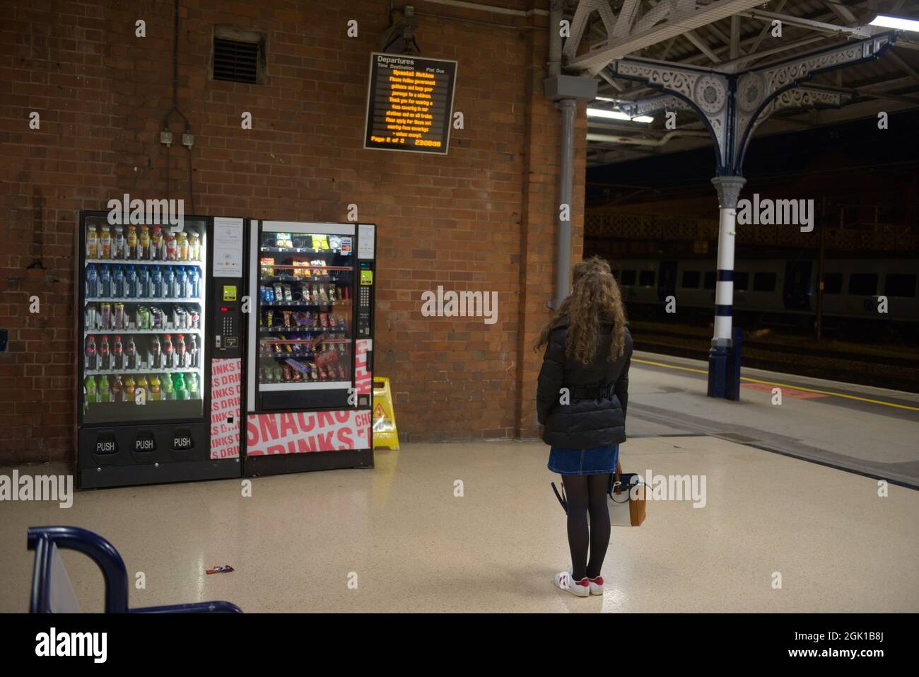 Doncaster, Großbritannien, 22. Mai 2021: Frau mit langen lockigen Brünetten Haaren und Winterkleidung erwägt, bei welchem Verkaufsautomaten sie kaufen soll Stockfoto