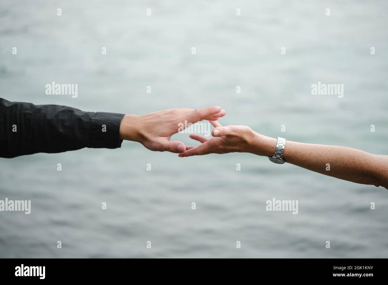 Mann und Frau strechen sich gegenseitig aus und halten die Hände über grauem, monochromen Wasser. Beziehungen, Wiedervereinigung, Liebe, Unterstützung, Verbindungskonzept. Kopieren Stockfoto