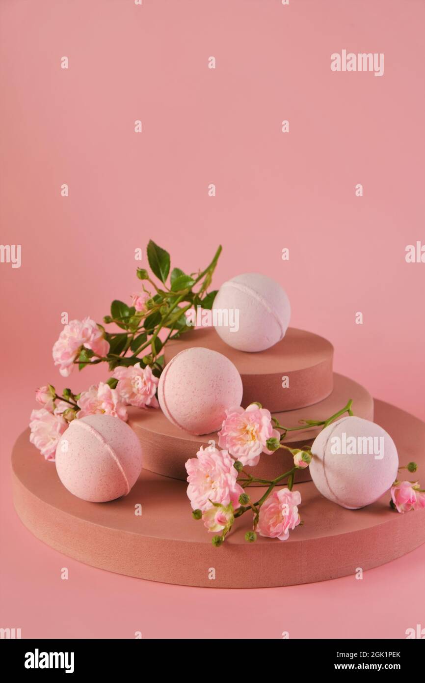 Badebomben mit Rosenextrakt. Badebomben und rosa Rosenblüten auf burgunderrotem Sockel auf einer rosa background.Organic veganen Kosmetik. Naturkosmetik Stockfoto