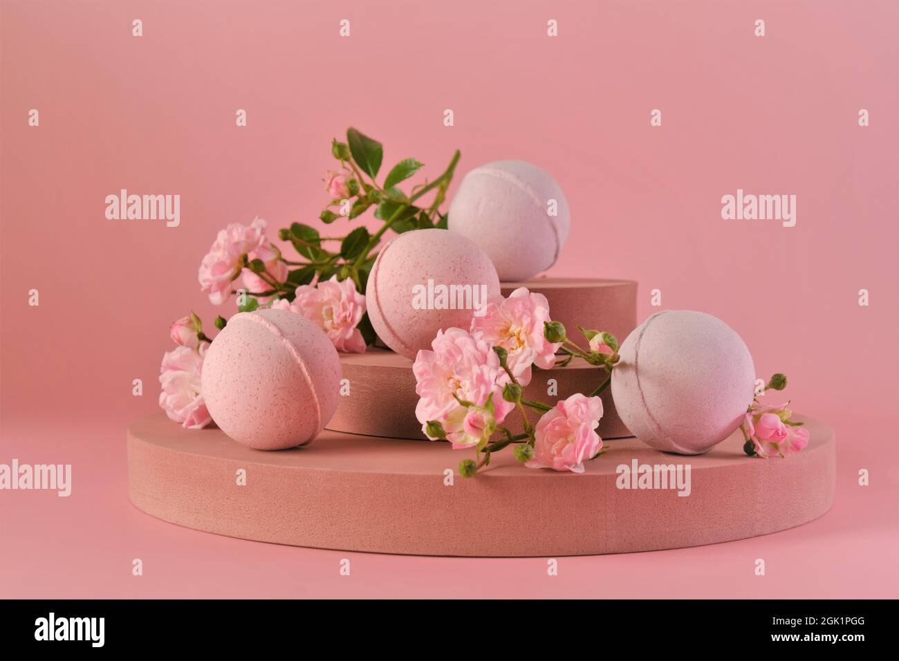 Badebomben mit Rosenextrakt.Rosa Badebomben und rosa Rosenblüten auf burgunderrotem Sockel auf einer rosa background.Organic Kosmetik. Naturkosmetik mit Stockfoto