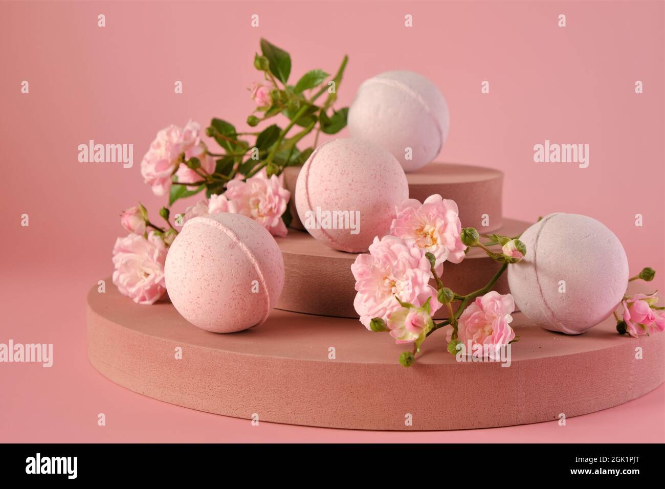 Badebomben mit Rosenextrakt.Rosa Badebomben und rosa Rosenblüten auf burgunderrotem Sockel auf einer rosa background.Organic veganen Kosmetik. Natürlich Stockfoto