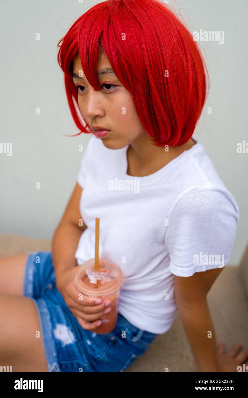 Rote Blutkörperchen Cosplay Schauspielerin sitzend trinken eine Smoothie | asiatische Teenage-Mädchen in roten Perücke Stockfoto