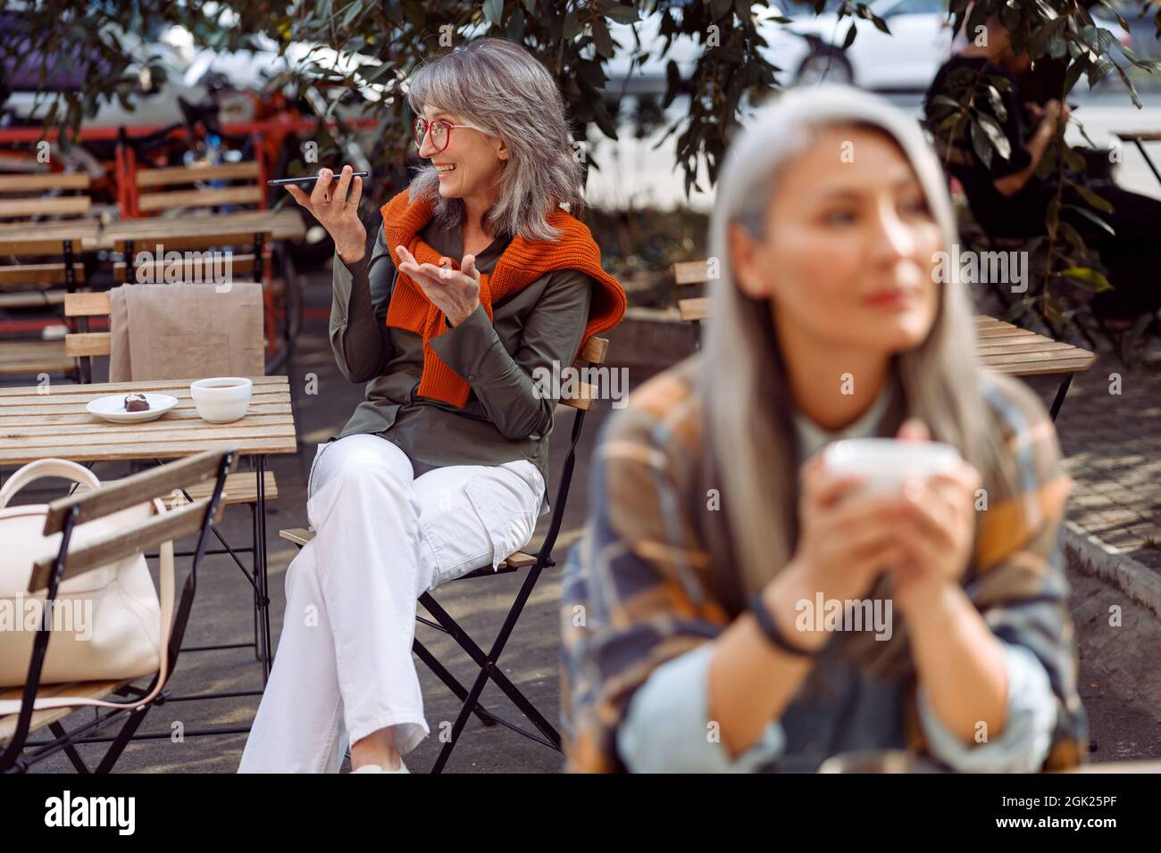 Ältere Cafe-Gäste, konzentrieren sich auf eine silberhaarige Frau mit einer Brille, die Audionachrichten aufzeichnet Stockfoto