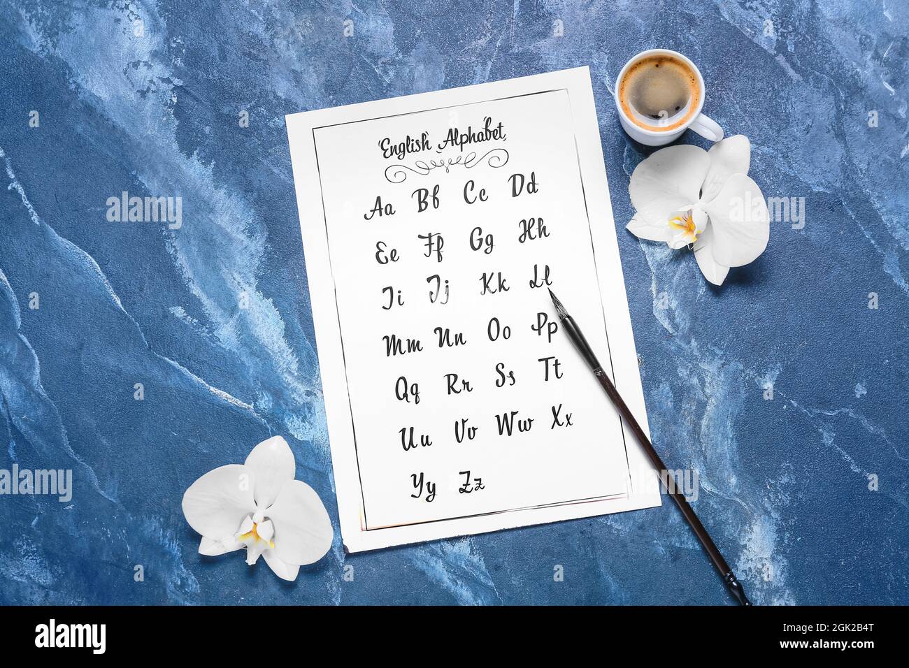 Papier mit Alphabet, Pinsel, Blumen und Tasse Kaffee auf blauem Hintergrund Stockfoto