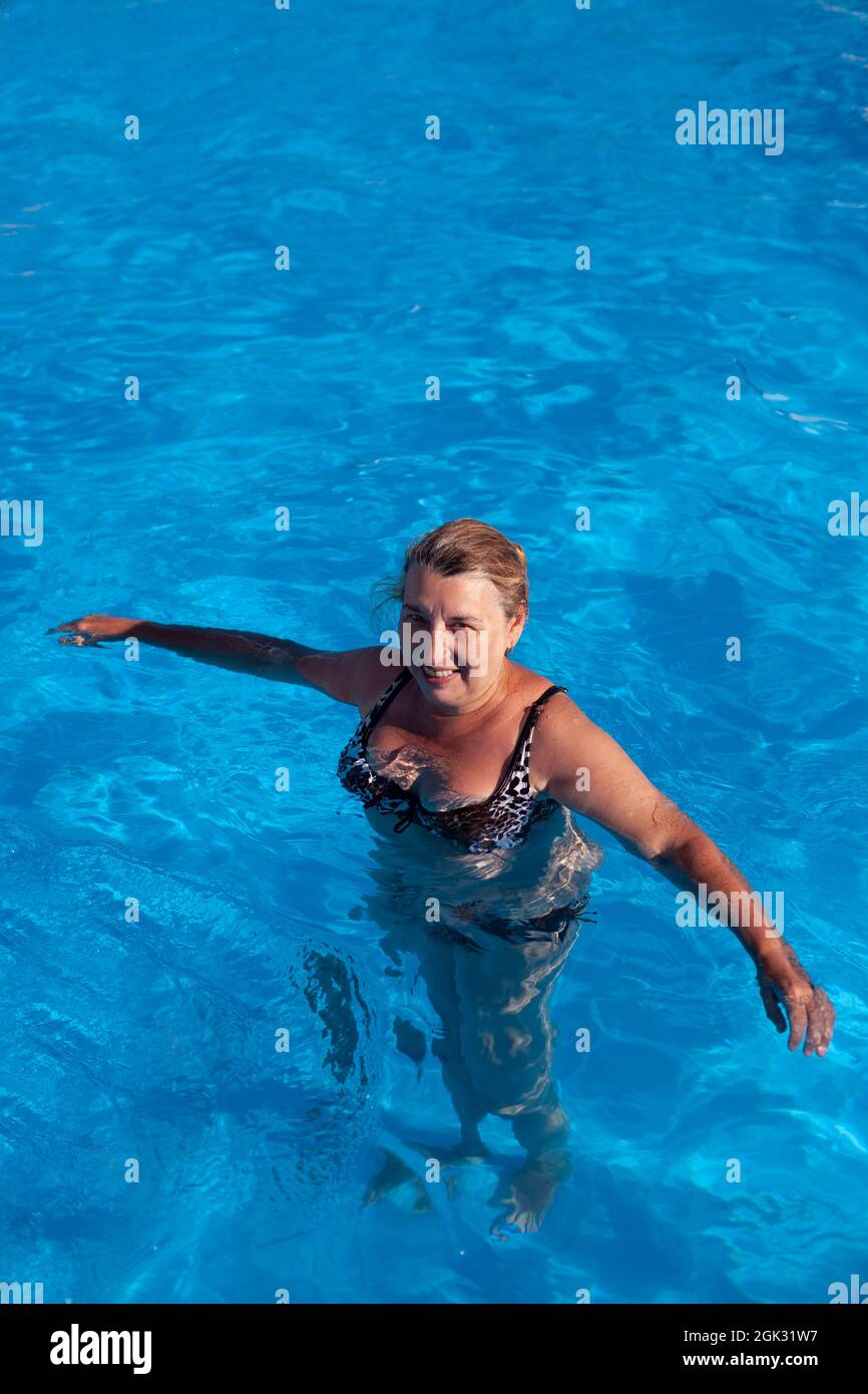 Die Frau steht im Wasser. Blonde mit nassem Haar im schönen Badeanzug steht im Pool und schaut in die Kamera Stockfoto