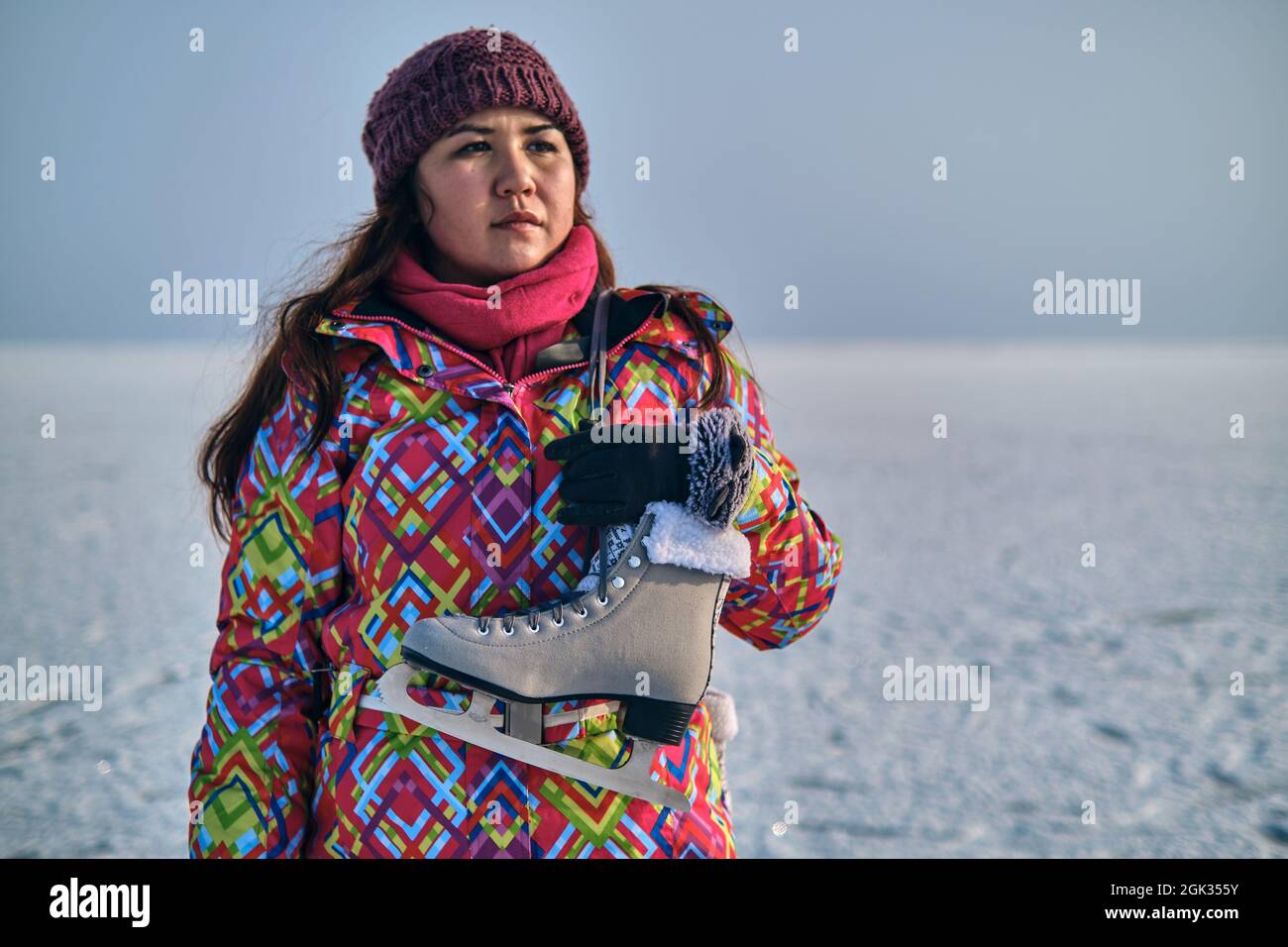 Eine Frau in einem Skianzug hält Schlittschuhe auf ihrer Schulter und blickt in die Ferne, nachdem sie auf einem gefrorenen See Skifahren konnte Stockfoto