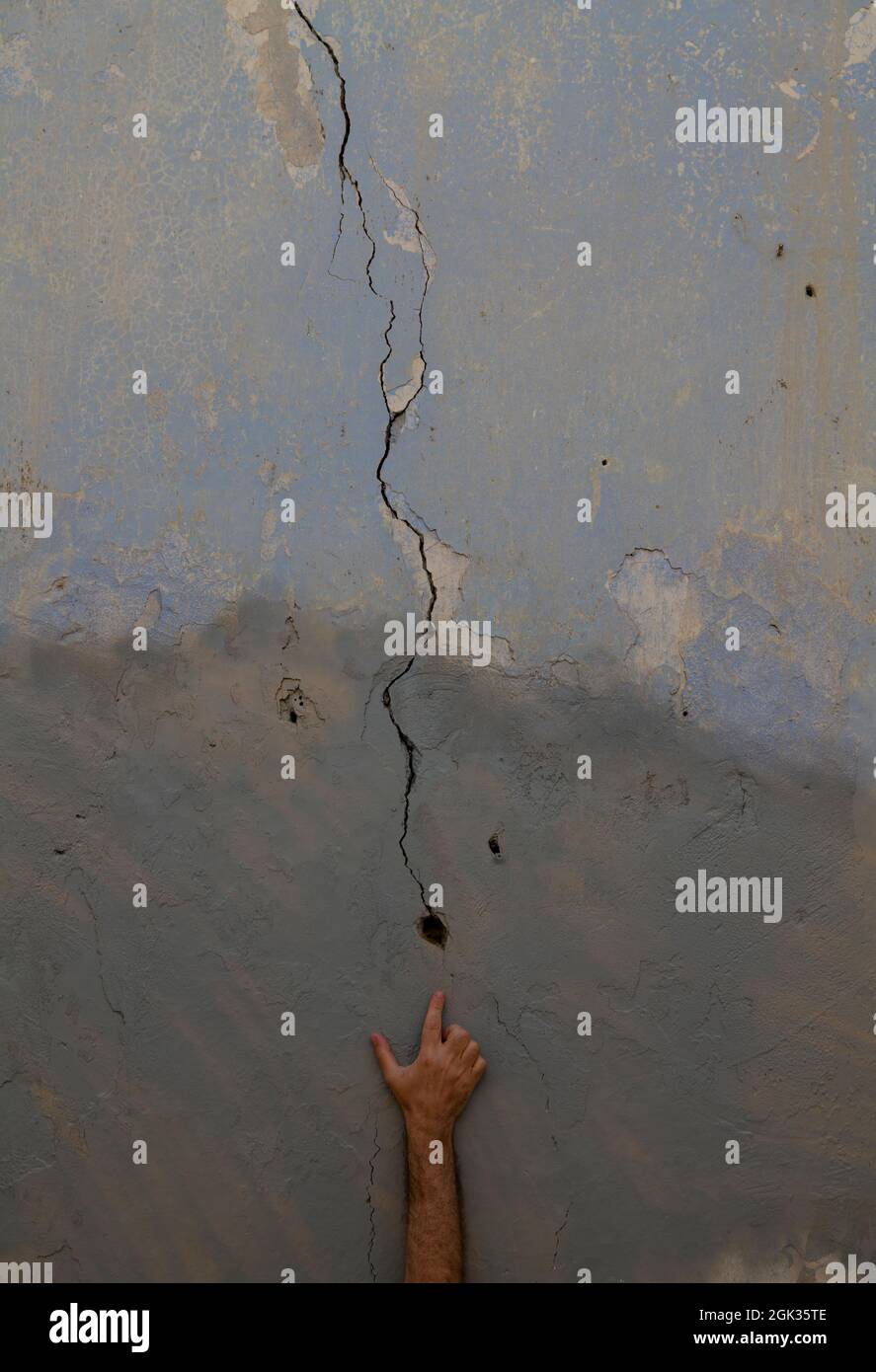 Hand zeigt auf ein Riss-Loch in der alten Wand Stockfoto