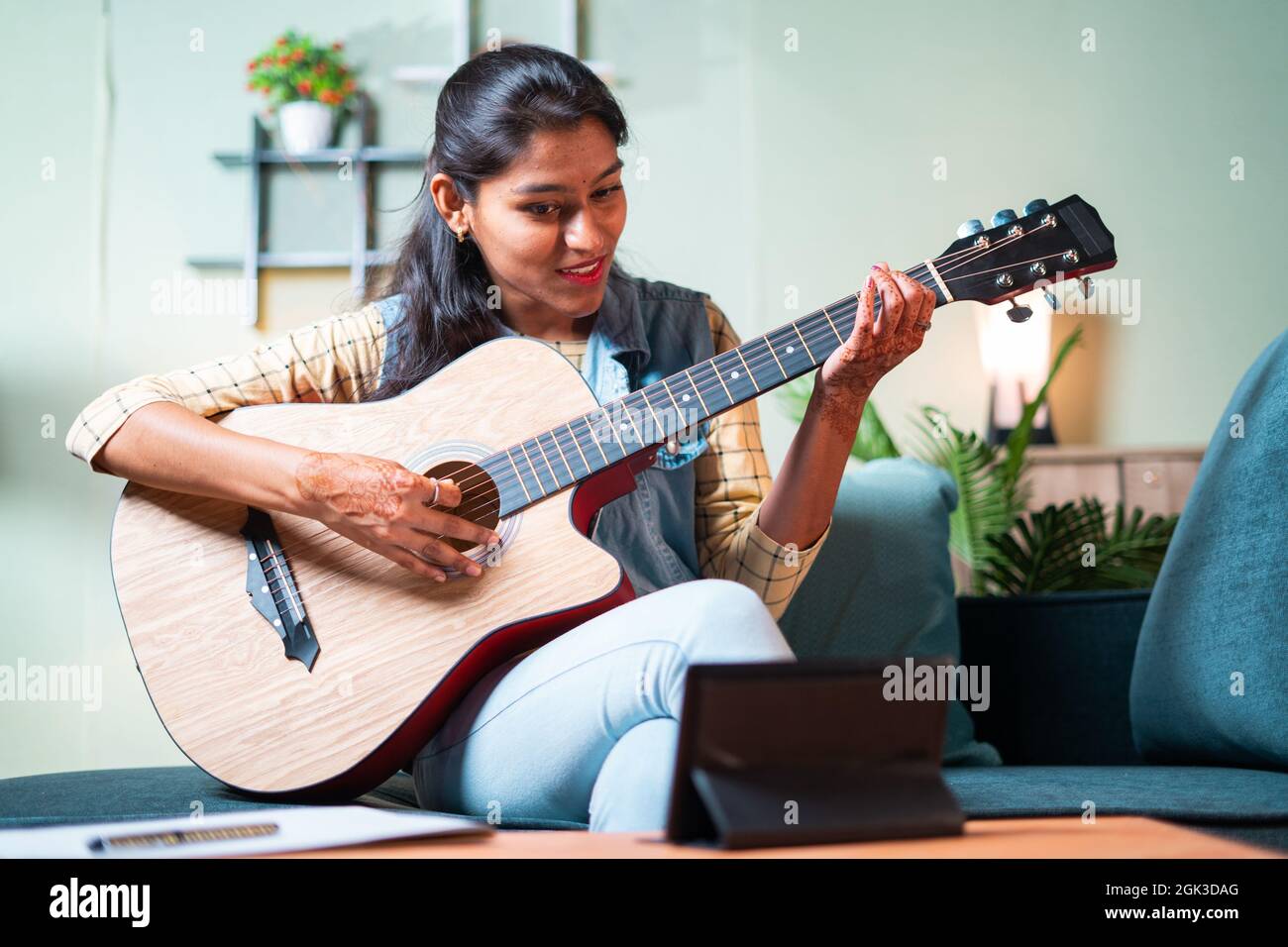 Junges Mädchen zu lernen, akustische Gitarre zu Hause von digitalen Tablet durch Videoanruf spielen - Konzept der neuen normalen, Online-oder virtuellen Bildung während Stockfoto