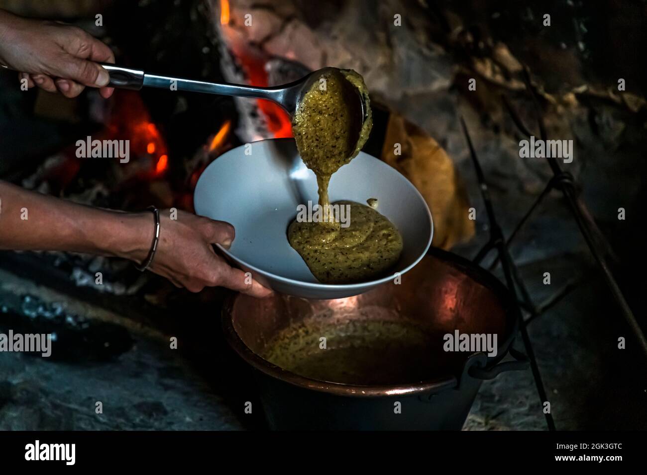 Eine Kelle gießt Polenta aus dem Kupferkessel in eine Schüssel am offenen Feuer von Cà Vegia in Cerentino. Das um 1600 erbaute Patrizierhaus verzichtet bewusst auf Elektrizität. Circolo della Rovana, Tessin, Schweiz. Stockfoto