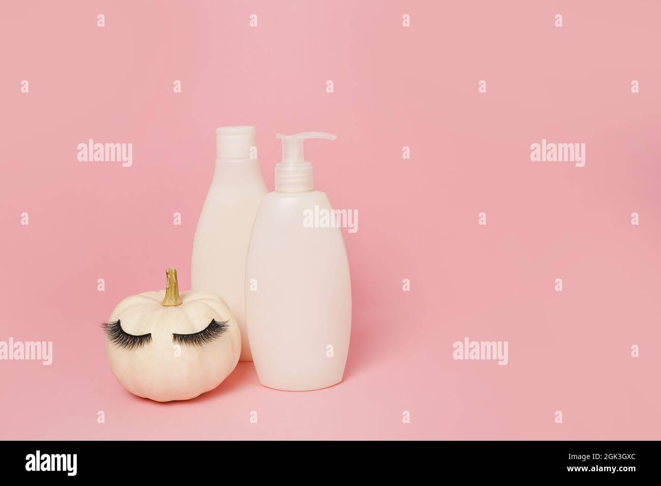 Kürbis mit falschen Wimpern und imitierten Kosmetikdosen Shampoo oder Gel auf rosa Hintergrund, natürliche Hautpflege im Herbst-Konzept Stockfoto