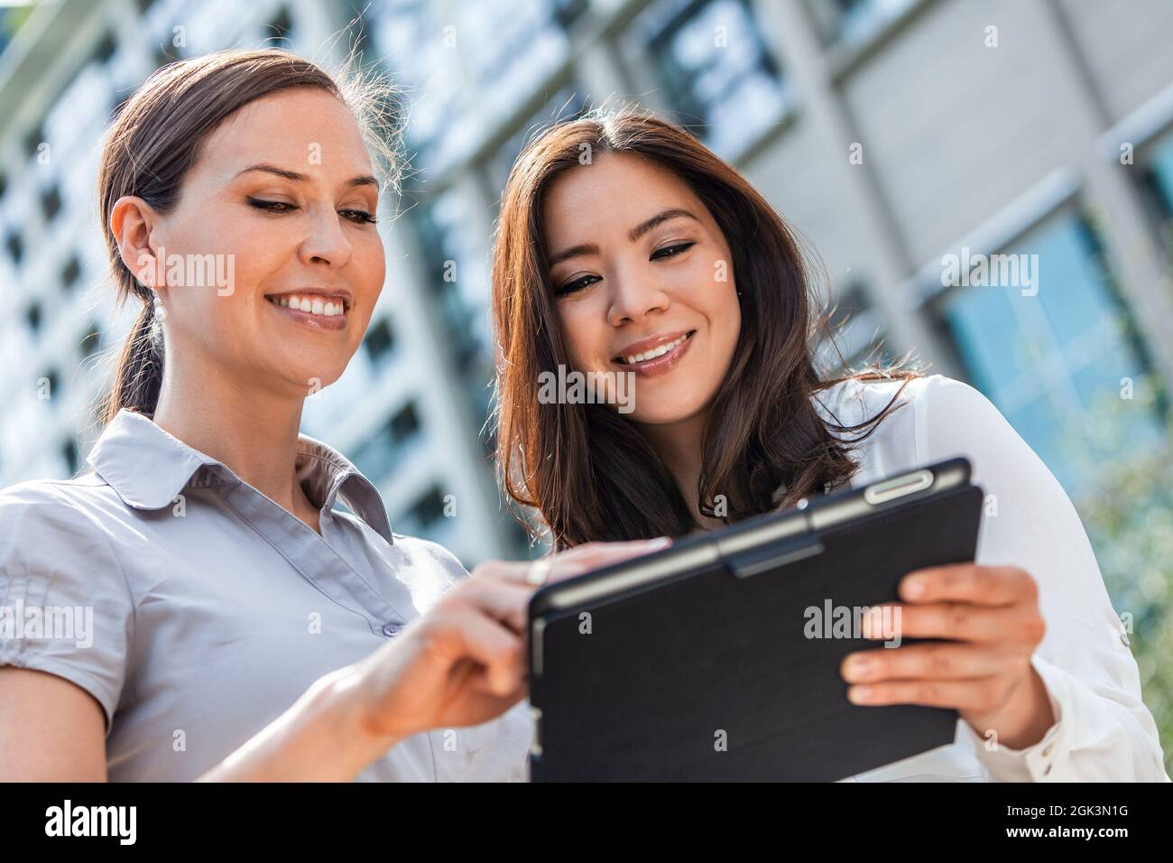 Business-Team aus zwei erfolgreichen Frauen, gemischte Rasse Gruppe von Geschäftsfrauen, Asiaten und Kaukasierinnen mit einem Tablet-Computer in einer modernen Stadt Stockfoto