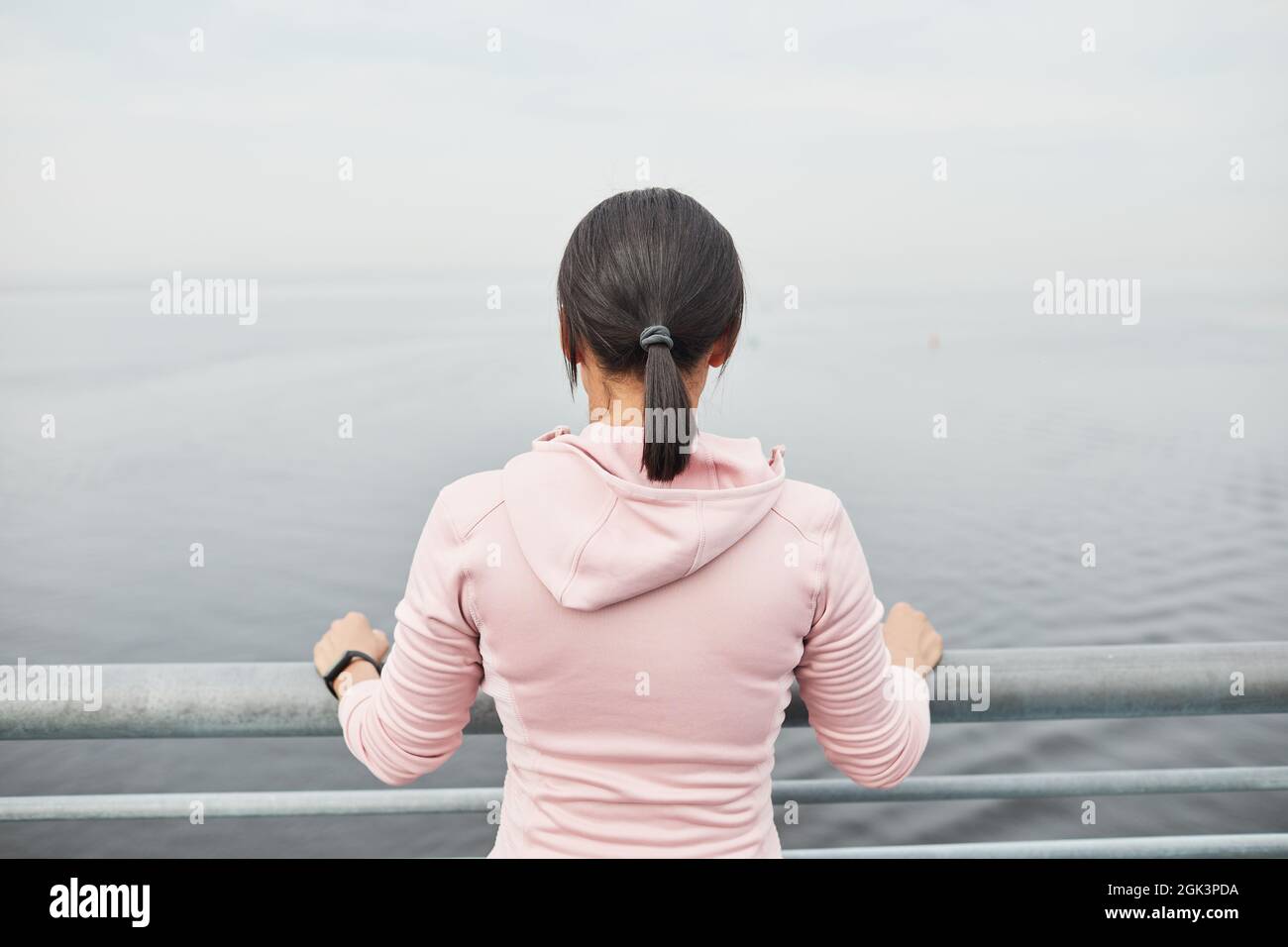 Rückansicht einer jungen Frau, die auf der Brücke steht und auf das wunderschöne Meer blickt Stockfoto