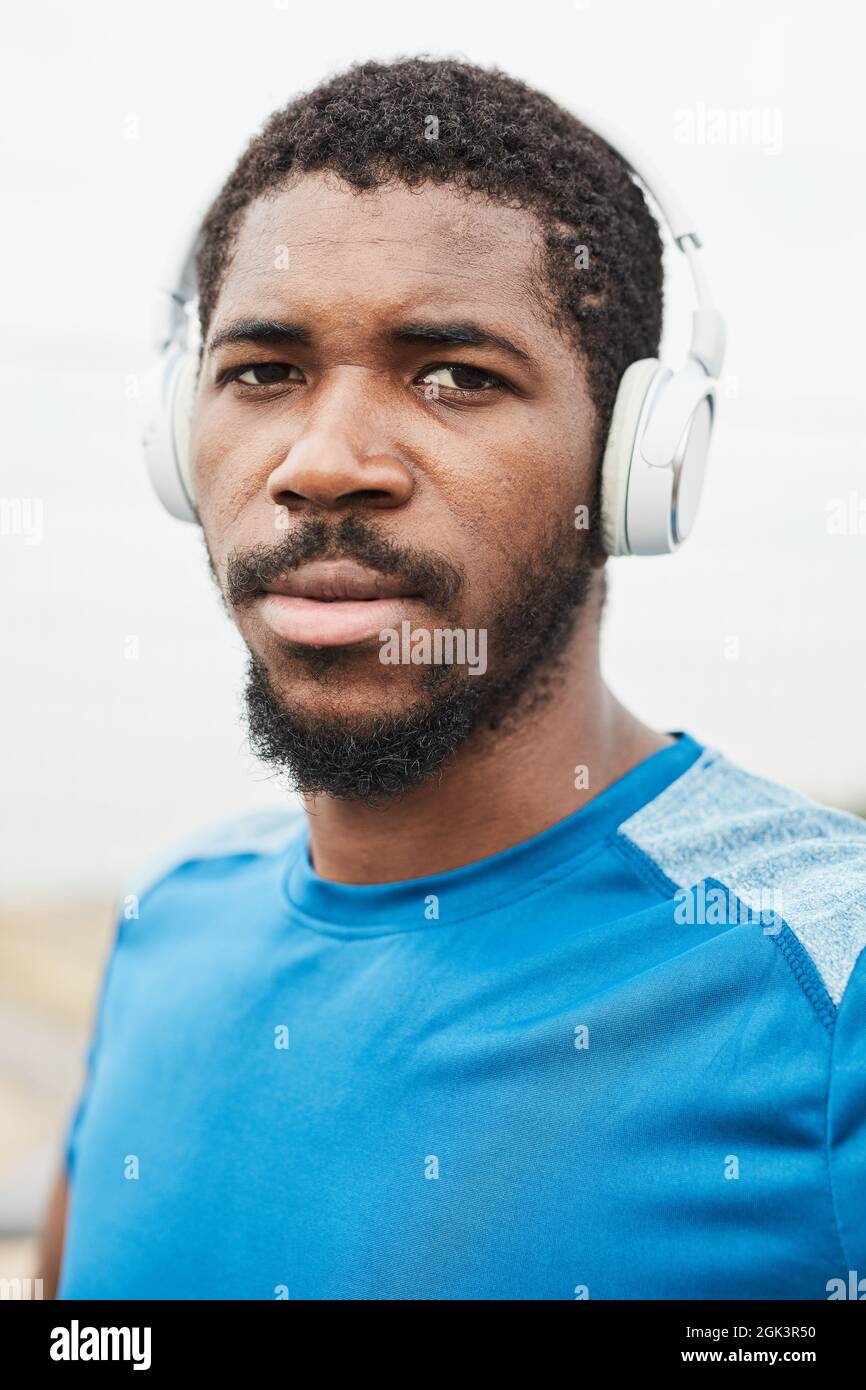 Porträt eines afrikanischen jungen Mannes in kabellosen Kopfhörern, der beim Musikhören auf die Kamera schaut Stockfoto