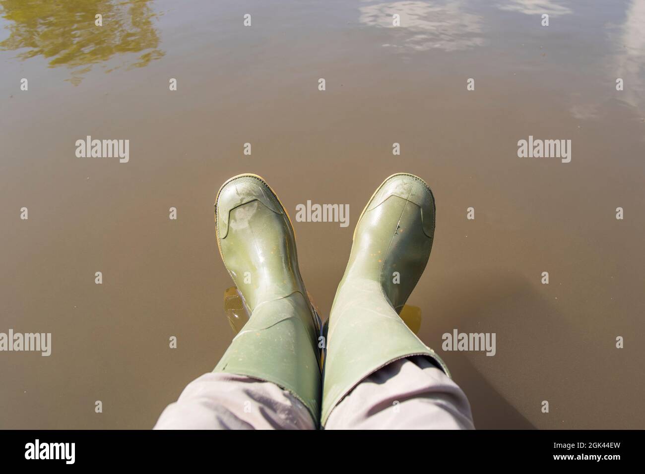 Draufsicht auf ein Paar grüne gummistiefel, die von einer Person über dem Wasser getragen werden. Stockfoto