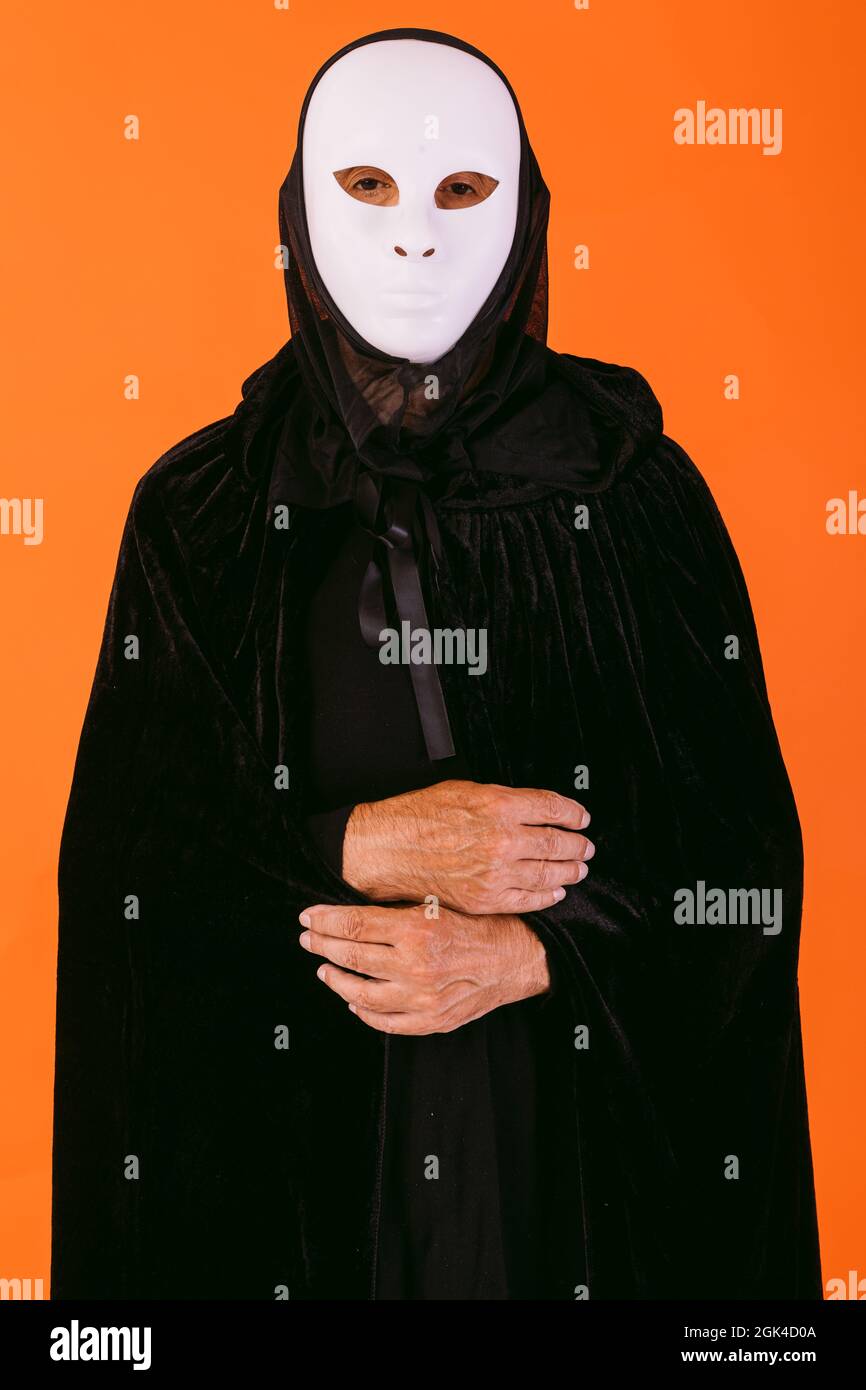 Porträt einer Person in weißer Killermaske, Umhang und Kapuze, die auf die  Kamera schaut, gekleidet für Halloween auf orangefarbenem Hintergrund  Stockfotografie - Alamy