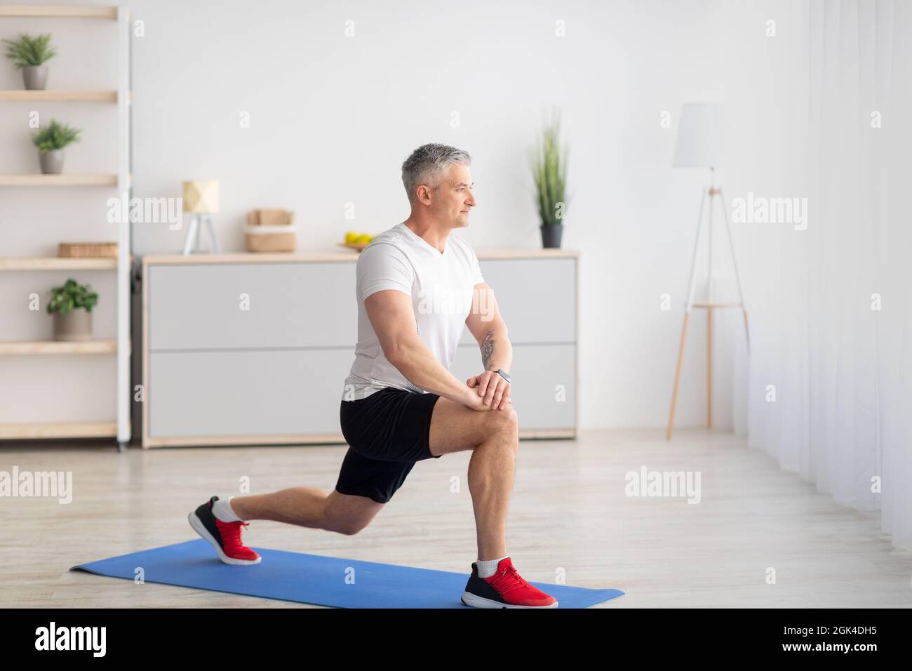 Heimfitness. Motivierter reifer Mann, der Ausfallschritte im Wohnzimmer, Freiraum, Bannerdesign macht Stockfoto