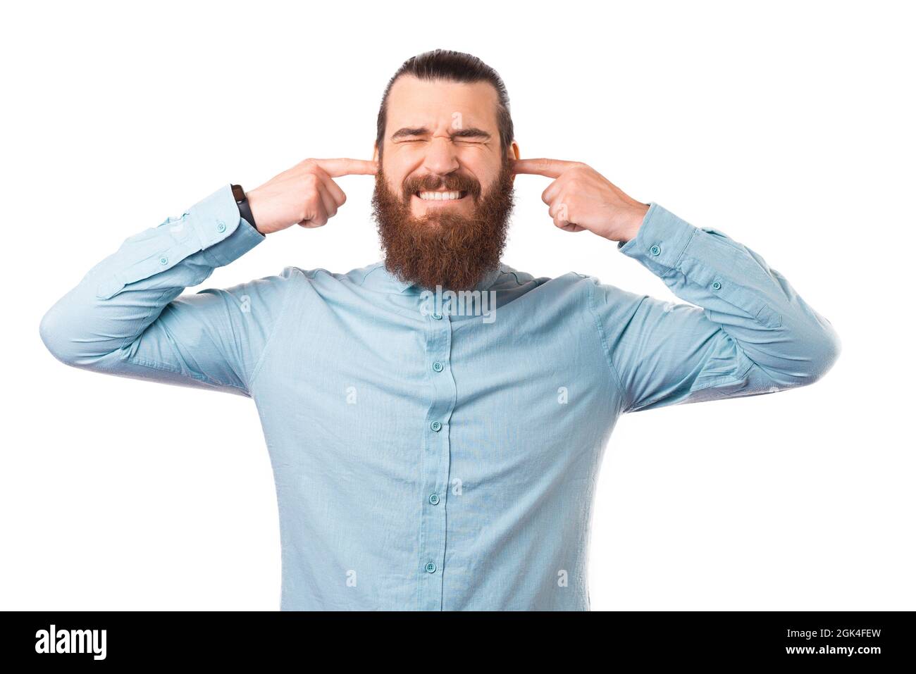 Der junge bärtige Mann schließt seine Ohren mit den Fingern über weißem Hintergrund. Stockfoto