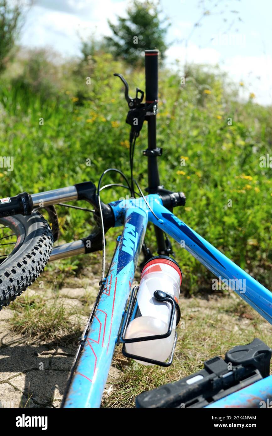 GÖTTINGEN, DEUTSCHLAND - 20. Aug 2021: Vertikale Aufnahme eines blauen Mountainbikes, das im Gras liegt und an dem eine Plastikwasserflasche befestigt ist. Außenspor Stockfoto