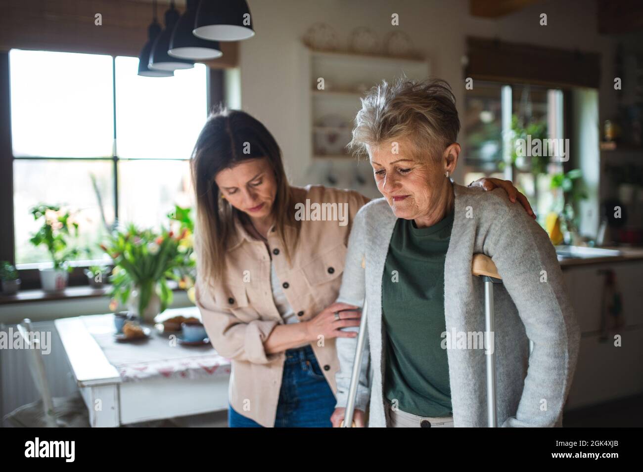 Erwachsene Tochter besucht kranke ältere Mutter mit Krücken zuhause und hält sie fest. Stockfoto