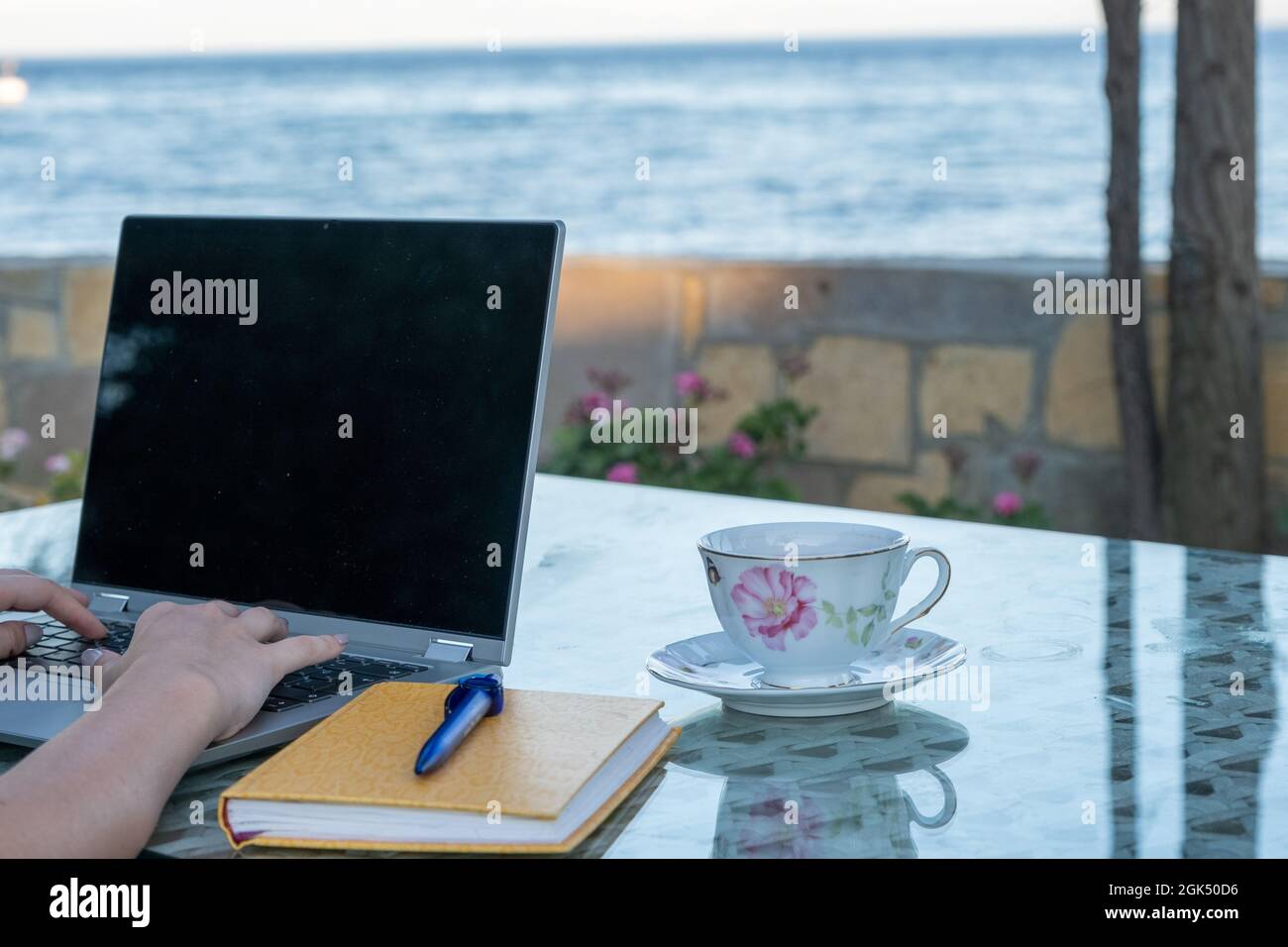 Frau, die am Meer am Laptop arbeitet und Kaffee trinkt, berufliches Fernarbeitsleben im Urlaub, Home Office Stockfoto