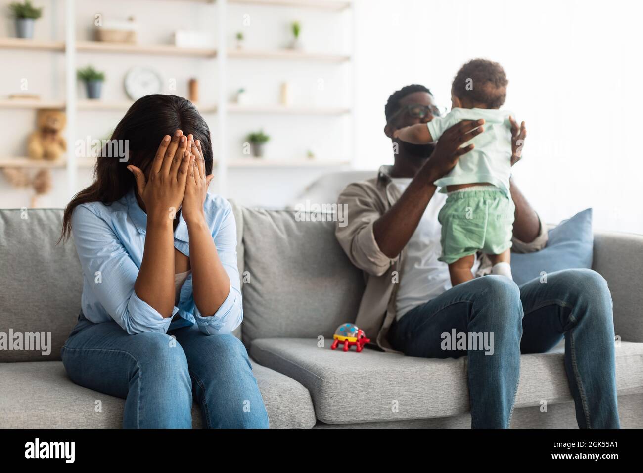 Müde afroamerikanische Mutter weint, Vater spielt mit Kind Stockfoto