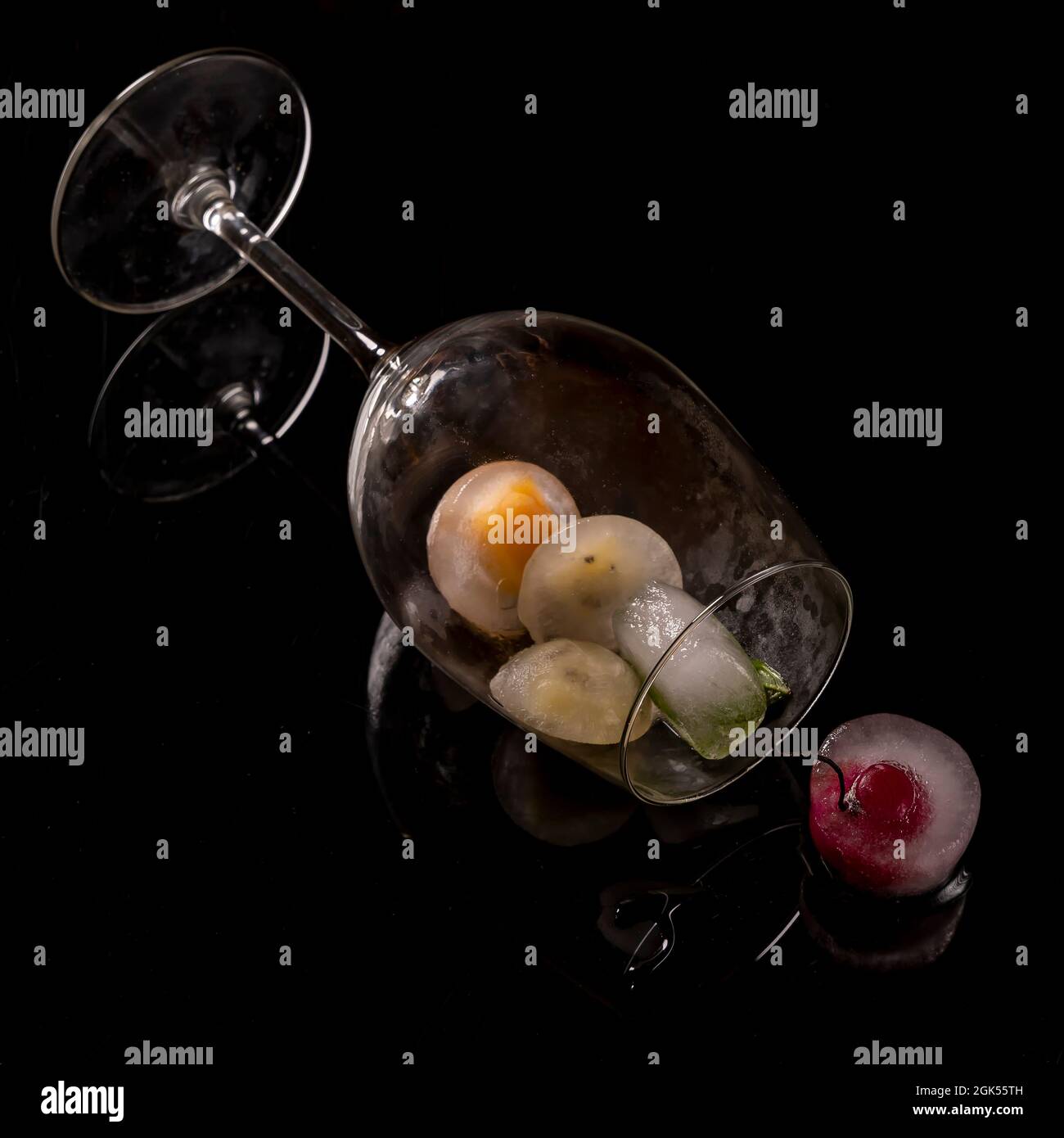 Ein Glas in horizontaler Position enthält Eiswürfel mit gefrorenen Früchten im Inneren Stockfoto