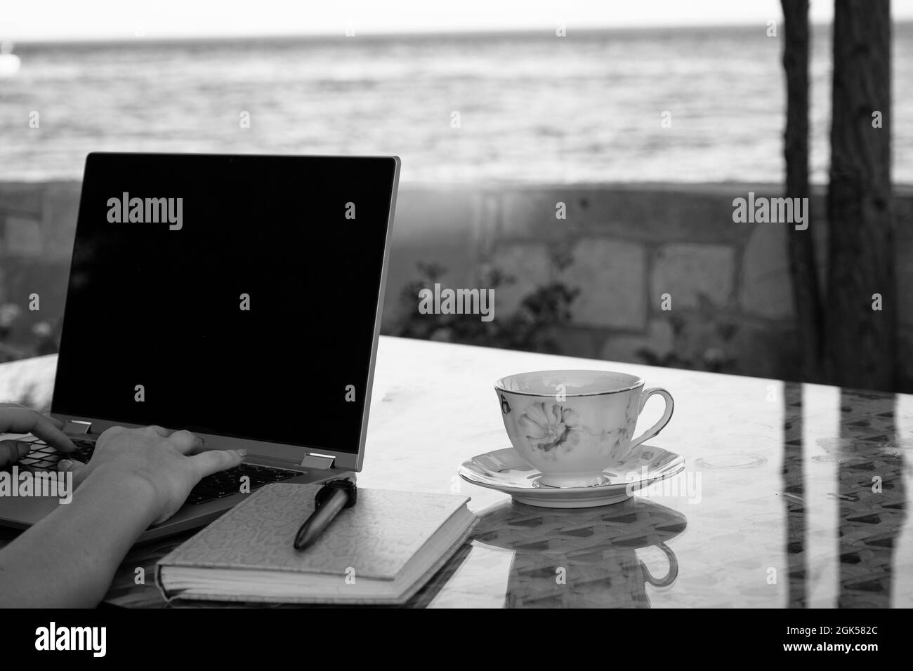 Frau, die am Meer am Laptop arbeitet und Kaffee trinkt, berufliches Fernarbeitsleben im Urlaub, Home Office Stockfoto