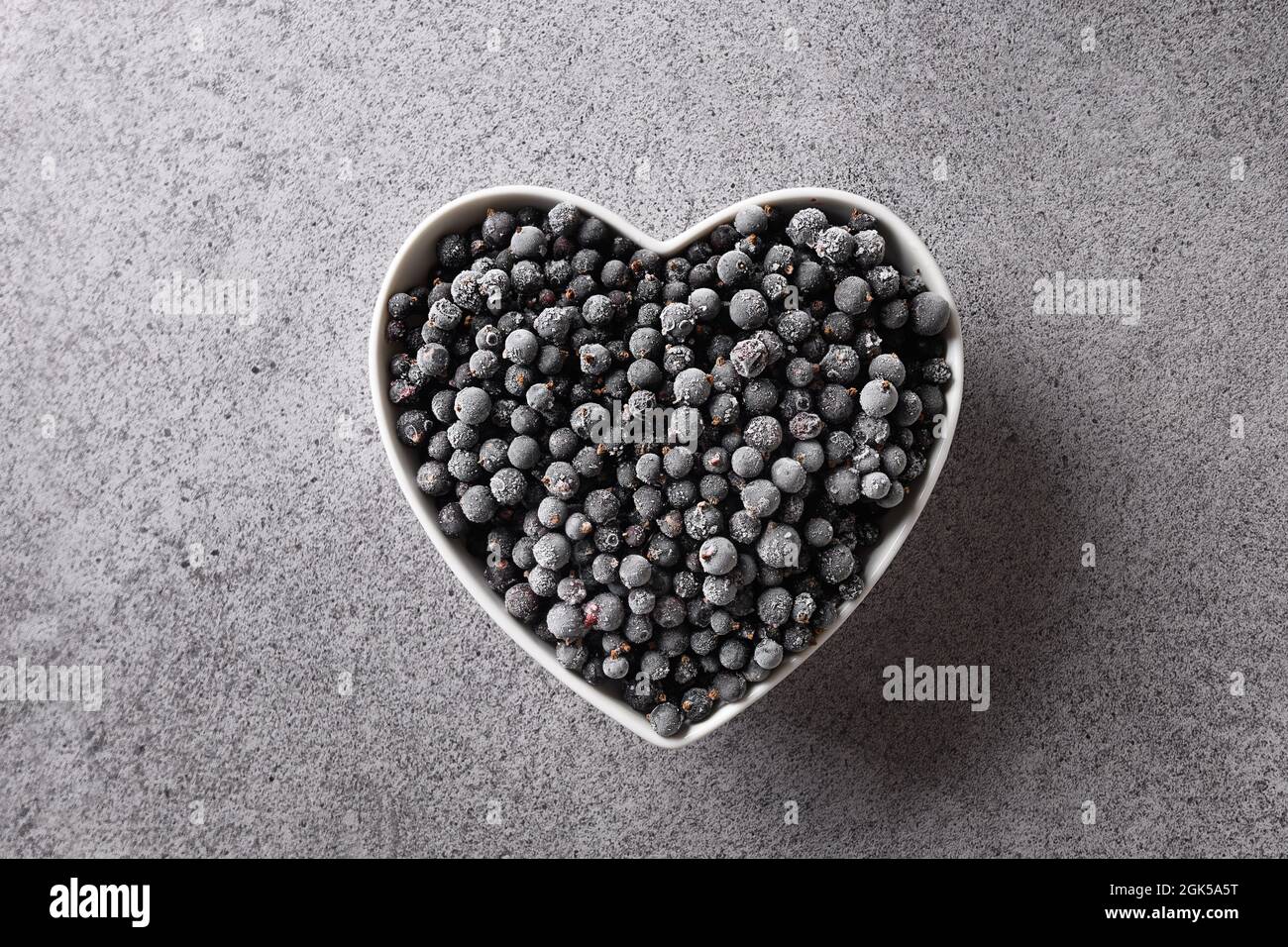 Gefrorene schwarze Johannisbeere in Platte geformt als Herz isoliert auf einem grauen Hintergrund. Blick von oben. Konzept Liebe Öko Bio-Lebensmittel. Stockfoto