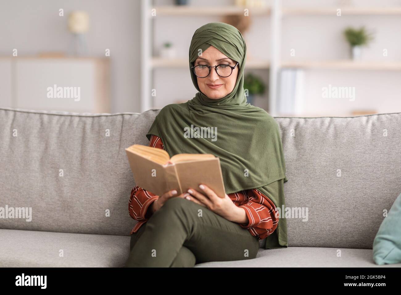 Glückliche Ältere Islamische Dame Liest Buch Mit Brille Zu Hause Stockfoto