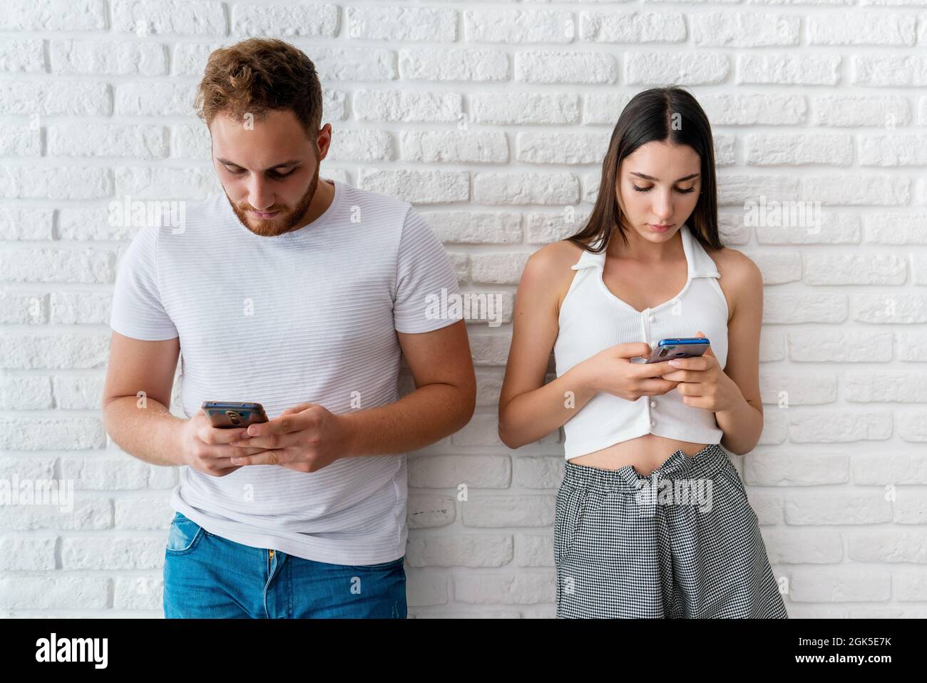 Zwei Freunde oder Liebhaber stehen vor der Awall und schauen auf ihre Handys. Konzept der Technologieabhängigkeit. Hochwertige Fotos Stockfoto