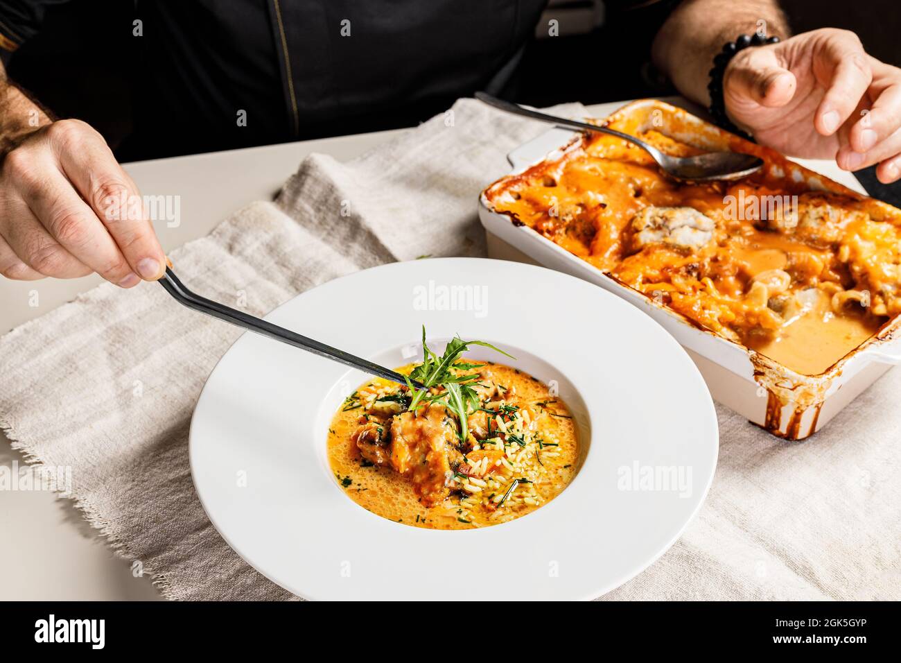 Authentische spanische Paella mit Kabeljau und Muscheln. Traditionelles mediterranes Seafood-Gericht. Der Koch schmückt das Gericht mit Kräutern mit einer Pinzette. Restaurant Stockfoto