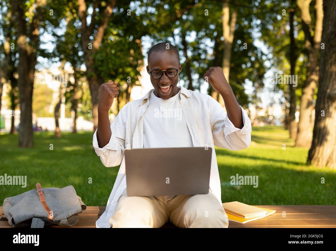 Fernschulungskonzept. Überglücklich schwarzer Mann mit Laptop-Computer gestikulierte JA im Freien, sitzt auf dem Campus der Universität Stockfoto