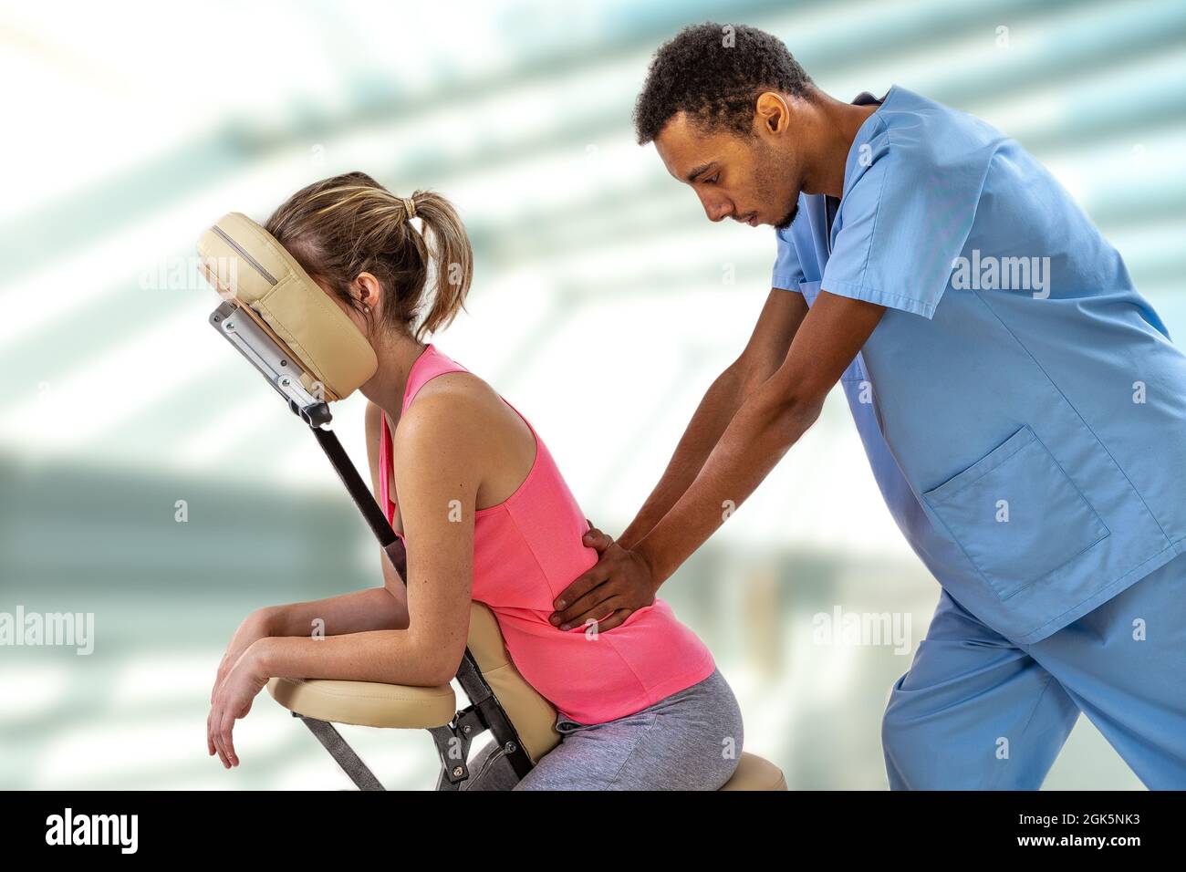 Physiotherapeut gibt einer Patientin, die in einem Massagesessel in der Klinik sitzt, eine Rückenmassage Stockfoto