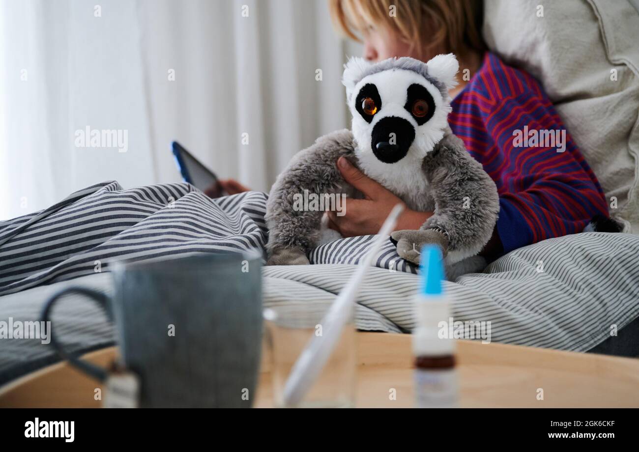 Berlin, Deutschland. September 2021. Ein Fieberthermometer, Nasenspray und eine Tasse Tee stehen vor einem Bett, in dem ein Kind mit einem Kuscheltier auf eine Tablette schaut. Quelle: Annette Riedl/dpa/Alamy Live News Stockfoto