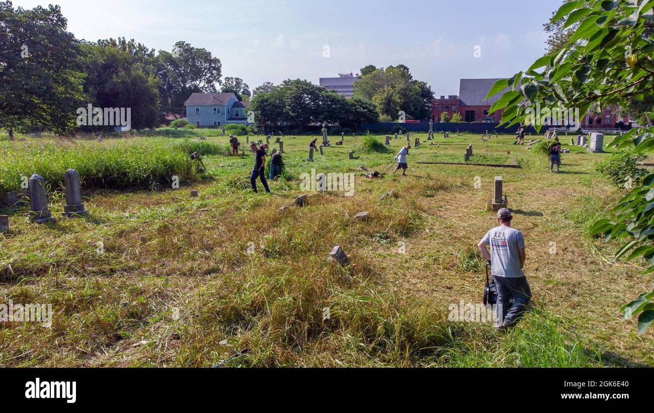 Soldaten der US-Armee und ihre Familien schneiden Gras auf dem historischen Elmerton Cemetery in Hampton, Virginia, während des 1. Bataillons, der monatlichen Veranstaltung des 210. Luftfahrtregiments „Unity Through Community“ am 14. August 2021. Bei dieser Veranstaltung werden Angehörige des Militärs mit Freiwilligen aus der Gemeinde zusammengebracht, die afroamerikanische Friedhofs restaurieren und gleichzeitig die Geschichte der Gegend von Hampton City hervorheben, das Vermächtnis der dort Vergrabenen ehren und die militärische Botschaft der Vielfalt, der Einbeziehung und des Respekts verbreiten. Stockfoto